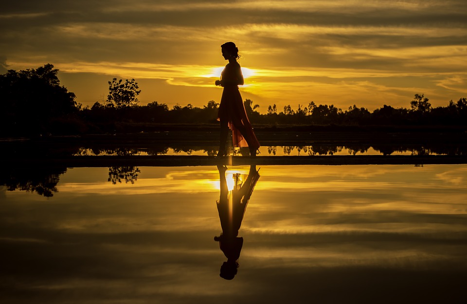 Image of a woman walking on the beach at sunset.